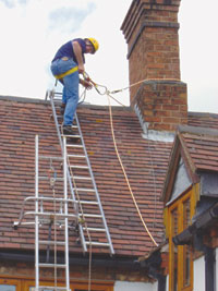 Engineer preparing to disconnect from ladder safety system to traverse chimney stack whilst attached to Chimney Strop via short cowstail webbing strop
